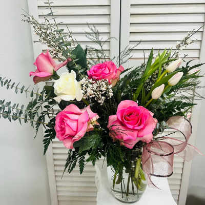 Pink and white roses arranged in a clear glass vase with a ribbon