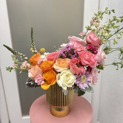 Mixed bouquet of pink, orange, and white flowers in a gold vase