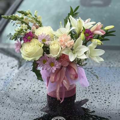 Bouquet of white lilies, roses, and pink daisies in a ribboned vase
