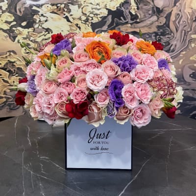 Mixed pink, purple, orange, and red flower arrangement in a gift box