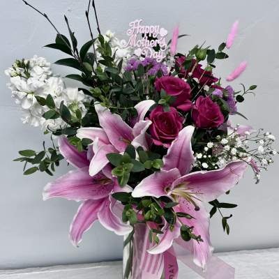 Pink lilies and roses in a glass vase with a Happy Mother's Day sign