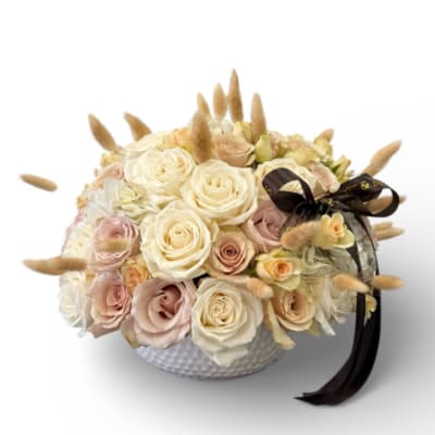 Cream and blush roses in a white textured bowl with a dark ribbon