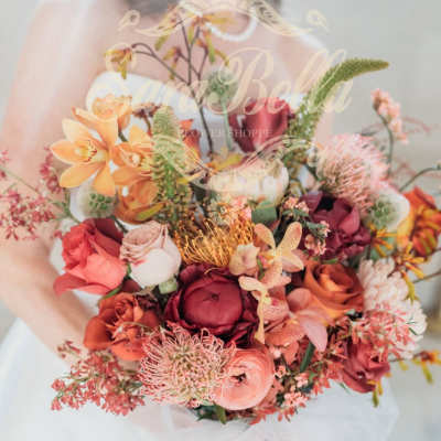 Handheld bouquet of orange, pink, and burgundy flowers