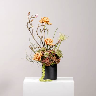 Tall floral arrangement with peach roses in a black vase