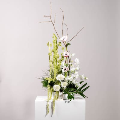 Tall floral arrangement with white and pale pink blooms in a white container
