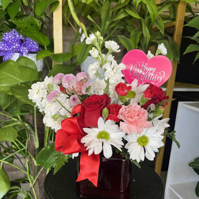 Mixed bouquet of red, pink, and white flowers in a dark vase with a heart sign