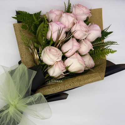 Bouquet of pale pink roses wrapped in gold paper with a green bow