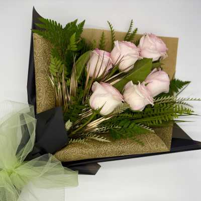 Bouquet of pale pink roses wrapped in patterned paper with a green tulle bow