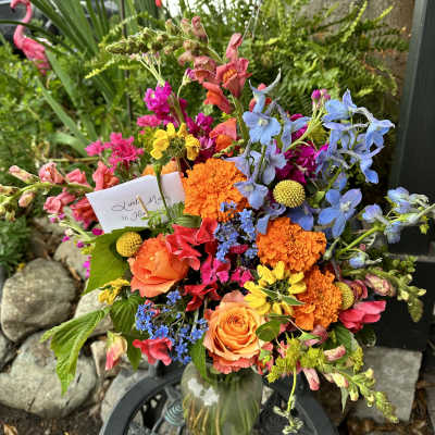 Colorful mixed bouquet in a glass vase with orange roses and blue flowers
