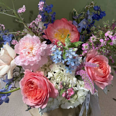 Bouquet of pink roses, peonies, and blue flowers in a wrapped arrangement