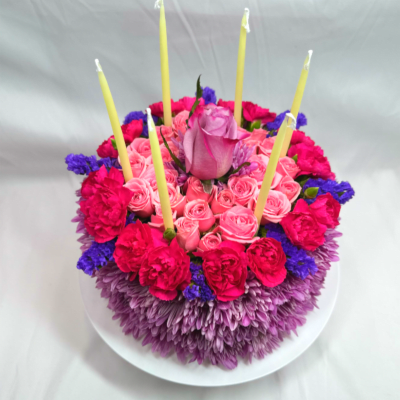 Round floral cake with pink roses and candles on a white plate