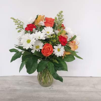 Mixed bouquet of orange roses, red carnations, and white daisies in a clear glass vase
