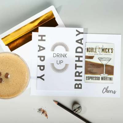 Birthday card reading Drink Up with gold-lined envelope and espresso martini drink mix packet.