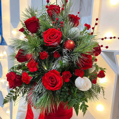 Red and white roses arranged with pine and berries in a red hatbox