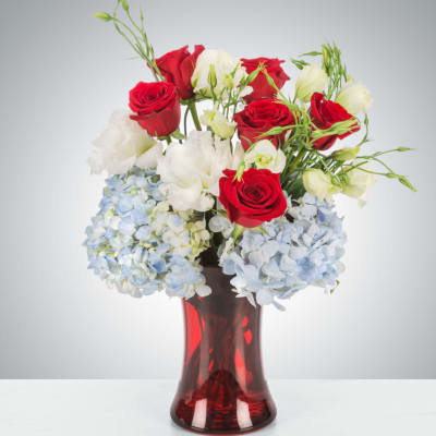 Red and white roses with blue hydrangeas in a red glass vase