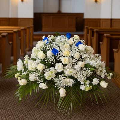 White floral arrangement with blue accents in a church aisle