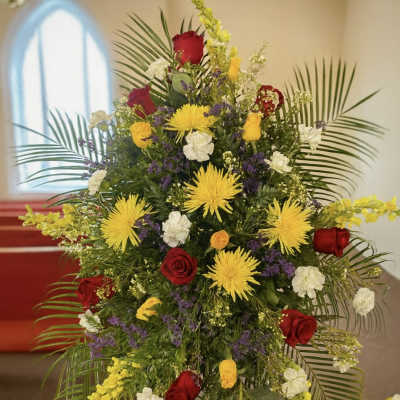 Tall funeral spray with red roses, yellow spider mums, and white carnations