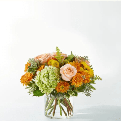 Mixed bouquet of peach roses, green hydrangea, and orange blooms in a glass vase