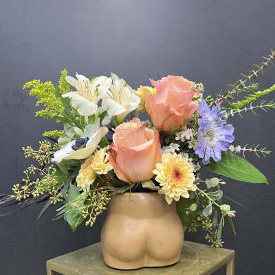Peach roses and mixed flowers in a tan ceramic vase shaped like a torso