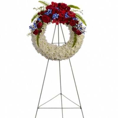 Floral wreath on a metal easel with red roses, white flowers, and blue accents