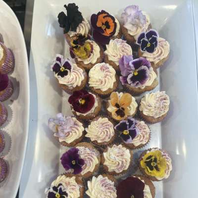 Tray of frosted cupcakes topped with colorful edible flowers