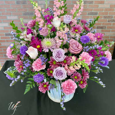 Large mixed bouquet in a white container with pink, lavender, and purple flowers