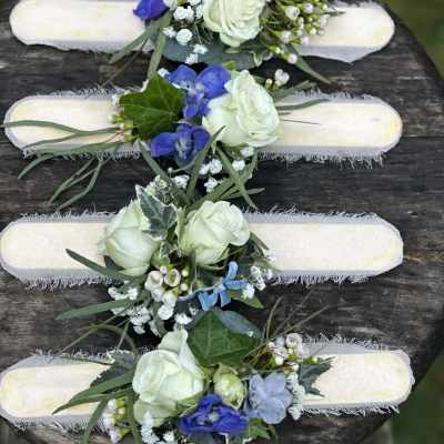 Four floral wrist corsages with white roses and blue flowers on pale bands