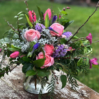 Pink roses and purple flowers in a clear glass vase with branches