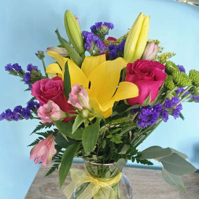 Bouquet of yellow lilies, pink roses, and purple filler flowers in a glass vase