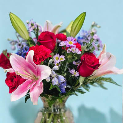 Bouquet of pink lilies, red roses, and purple daisies in a glass vase