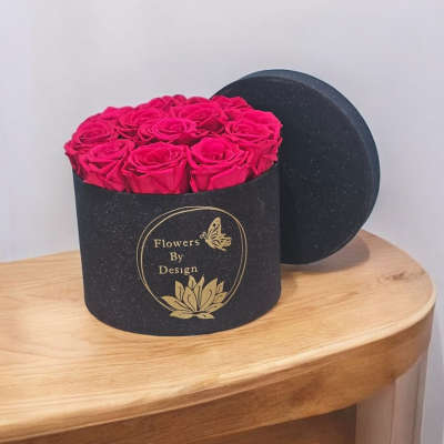 Pink roses in a black round gift box with a lid behind it