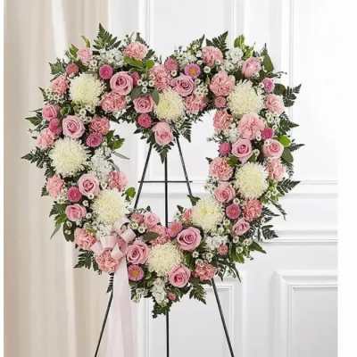 Heart-shaped floral wreath with pink roses and white blooms on a stand