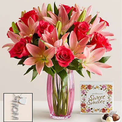 Pink lilies and red roses in a tall glass vase with a card and chocolates