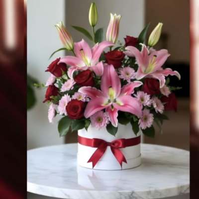Pink lilies and red roses in a white hatbox with a red ribbon