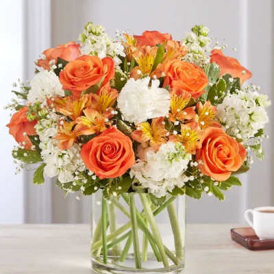 Orange roses and white flowers arranged in a clear glass vase