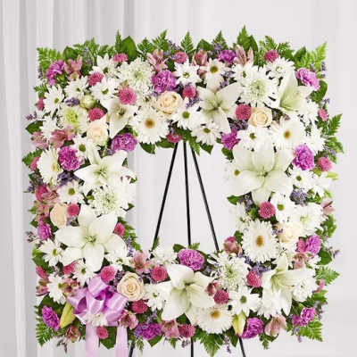 Floral wreath on a black stand with white and pink flowers and a lavender ribbon