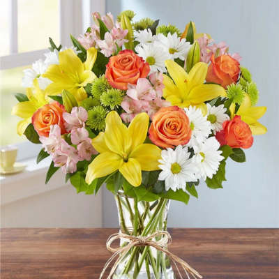 Bouquet of yellow lilies, orange roses, and white daisies in a glass vase