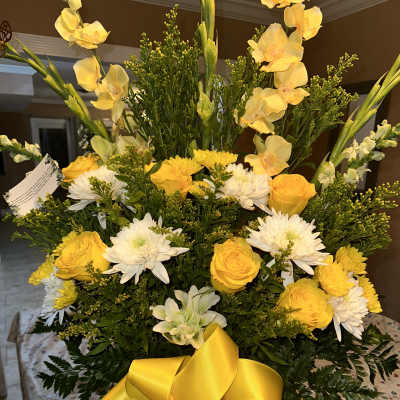 Yellow and white floral arrangement with a large yellow ribbon in a white vase