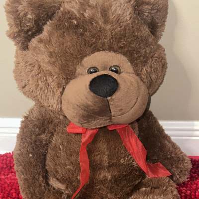 Brown teddy bear with a red ribbon sitting on a red textured surface