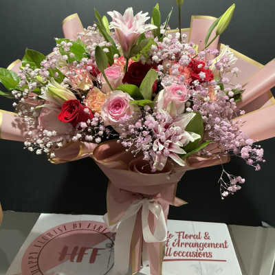 Pink and red mixed bouquet with lilies, roses, and baby's breath wrapped in pink paper