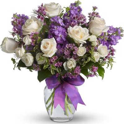 White roses and purple flowers in a glass vase with a purple ribbon