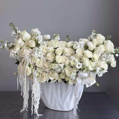 White roses and calla lilies arranged in a white vase