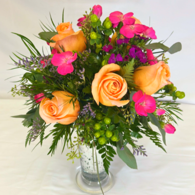 Peach roses and bright pink blooms arranged with berries in a clear glass vase.