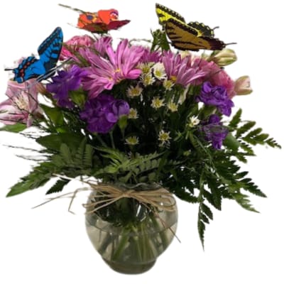 Mixed bouquet of purple and pink flowers in a glass vase with butterfly picks