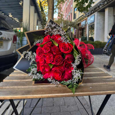 Bouquet of red roses with white filler flowers wrapped in black paper on a wooden outdoor table