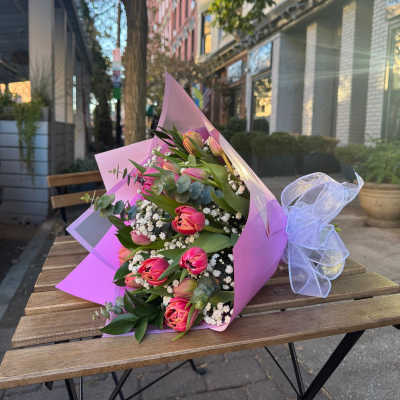 Pink tulip bouquet with white filler flowers wrapped in pink paper and ribbon on a café table