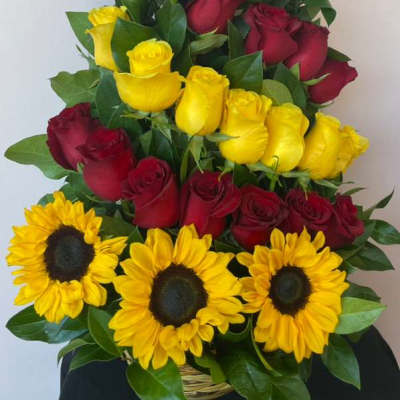 Tall arrangement of red and yellow roses with yellow sunflowers in a basket