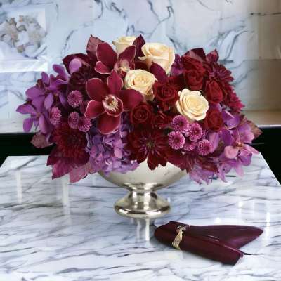 Bouquet of burgundy, purple, and cream flowers in a silver pedestal vase