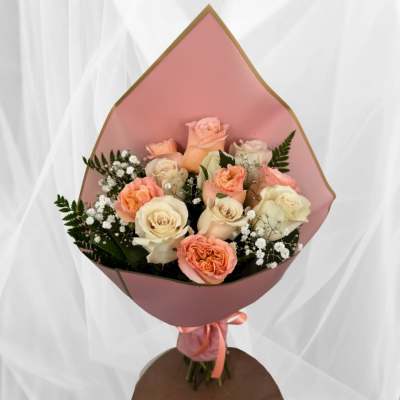 Bouquet of peach and cream roses with white filler flowers wrapped in pink paper