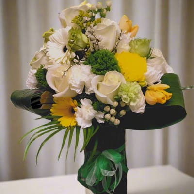 Bouquet of white and yellow flowers with green accents in a black wrap